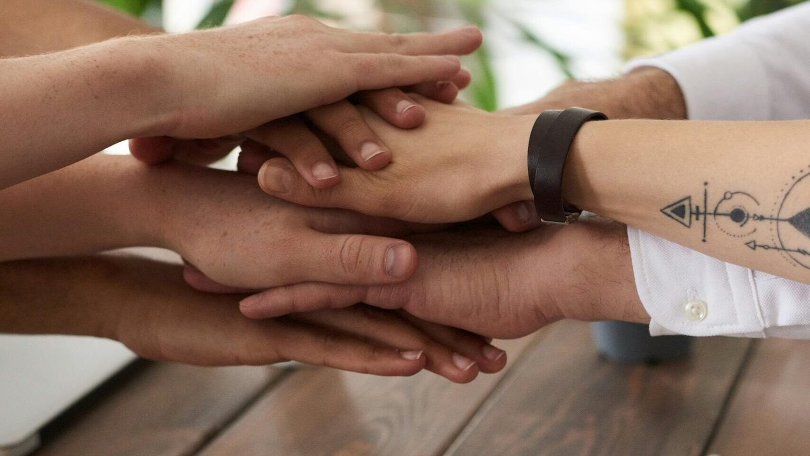 Hands from a diverse team stack on a table symbolizing unity and teamwork in a modern office setting.